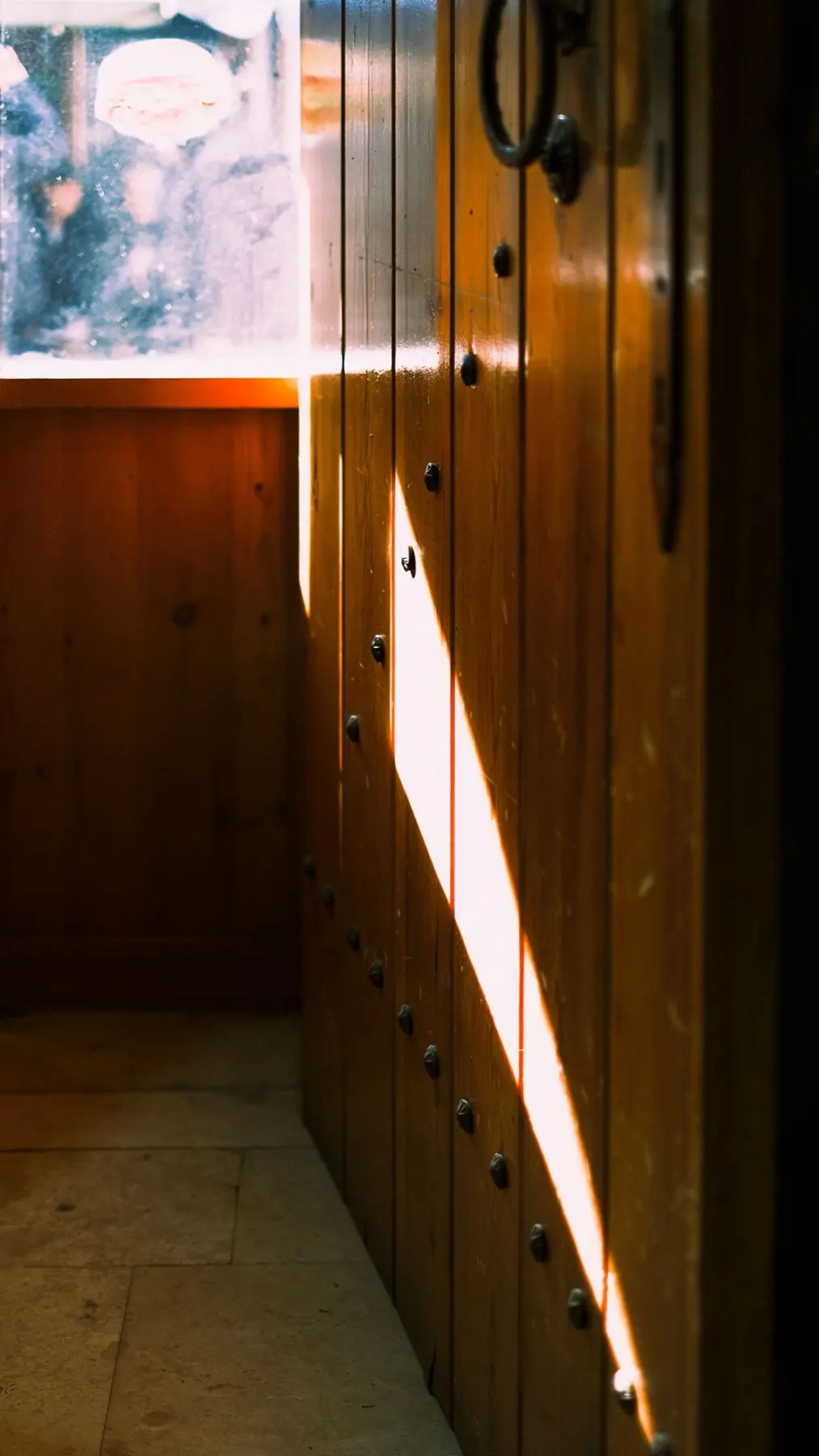 A timber plank door studded with iron, a band of daylight falling across it.